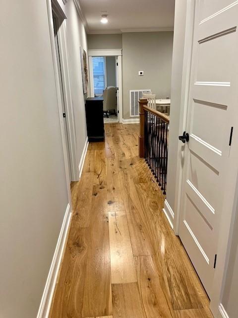 corridor featuring baseboards, light wood-type flooring, visible vents, and crown molding