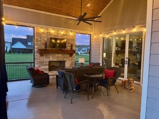 sunroom / solarium with lofted ceiling, wooden ceiling, ceiling fan, and an outdoor stone fireplace