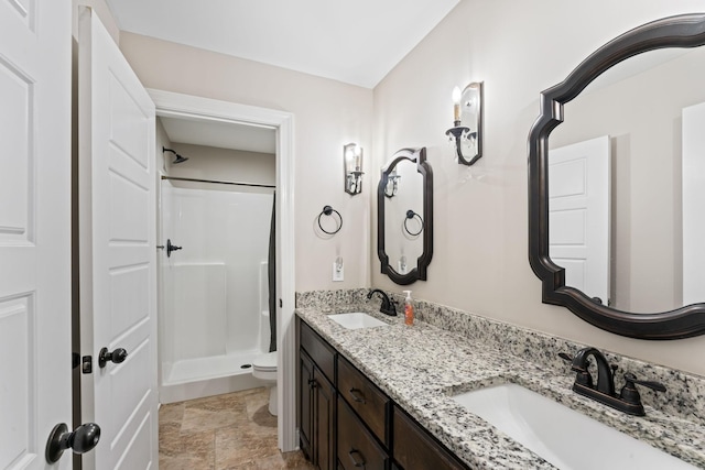 bathroom featuring toilet, a stall shower, double vanity, and a sink