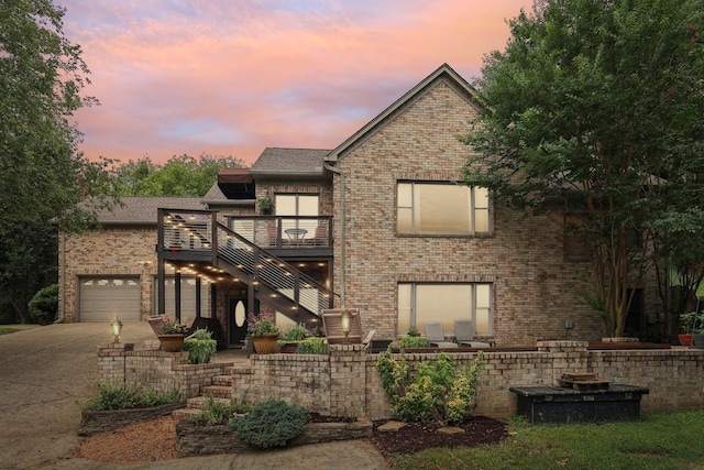 rear view of house featuring driveway, an attached garage, stairs, and brick siding