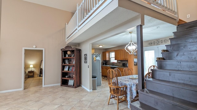 interior space featuring light tile patterned flooring, an inviting chandelier, a towering ceiling, and baseboards