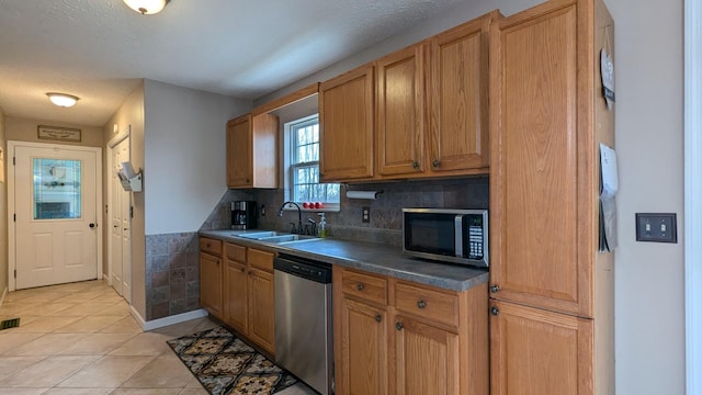 kitchen featuring brown cabinets, light tile patterned floors, stainless steel appliances, dark countertops, and a sink