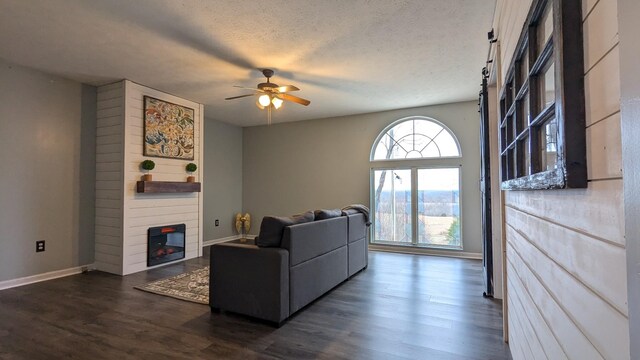 living area featuring baseboards, dark wood finished floors, ceiling fan, a textured ceiling, and a fireplace