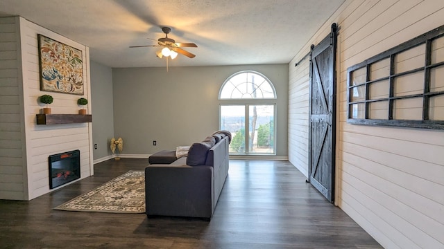 living area featuring a barn door, a glass covered fireplace, ceiling fan, wood finished floors, and a textured ceiling