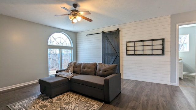 living area featuring dark wood-type flooring, a ceiling fan, baseboards, and a barn door