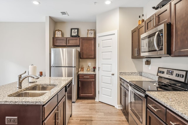 kitchen with light wood finished floors, dark brown cabinets, stainless steel appliances, and a sink