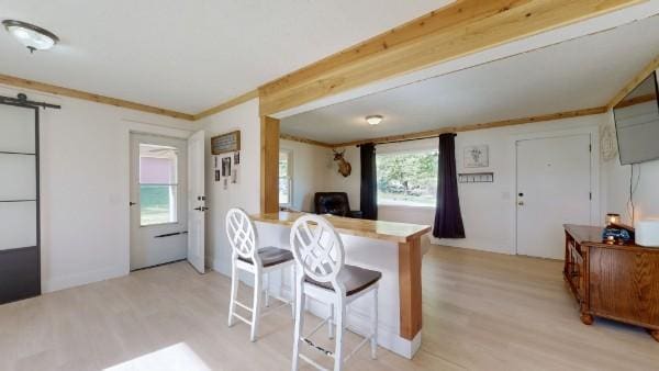 kitchen featuring light wood-style flooring, a kitchen bar, ornamental molding, and a barn door