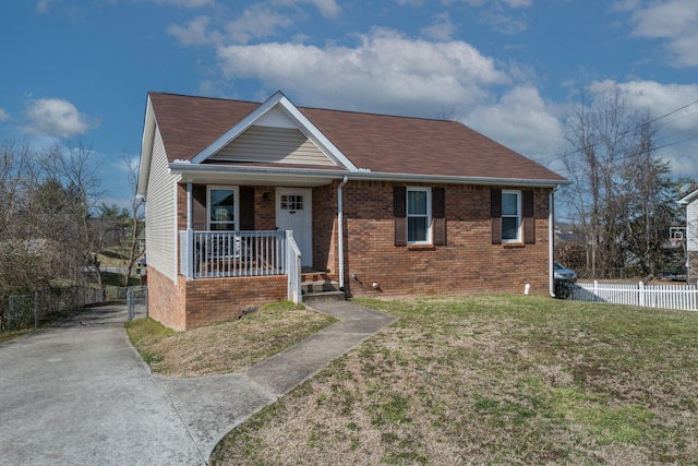 view of front of home featuring covered porch, brick siding, fence, roof with shingles, and a front lawn