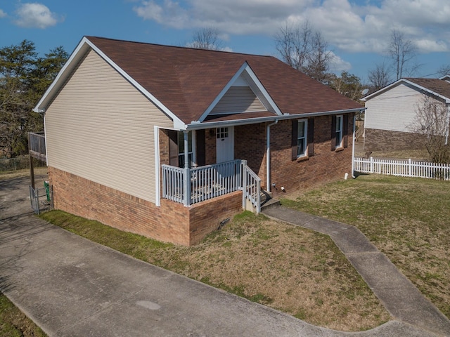 view of front facade with roof with shingles, covered porch, fence, a front lawn, and brick siding