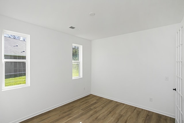 unfurnished room featuring dark wood-type flooring, visible vents, and baseboards