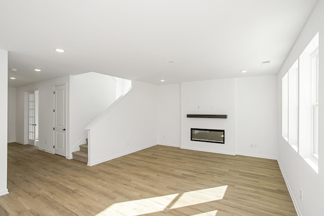 unfurnished living room with light wood-type flooring, recessed lighting, stairway, and a glass covered fireplace