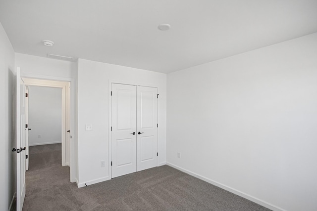 unfurnished bedroom featuring dark colored carpet, a closet, and baseboards