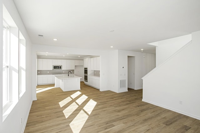 kitchen featuring visible vents, appliances with stainless steel finishes, a kitchen island with sink, light wood-type flooring, and a sink