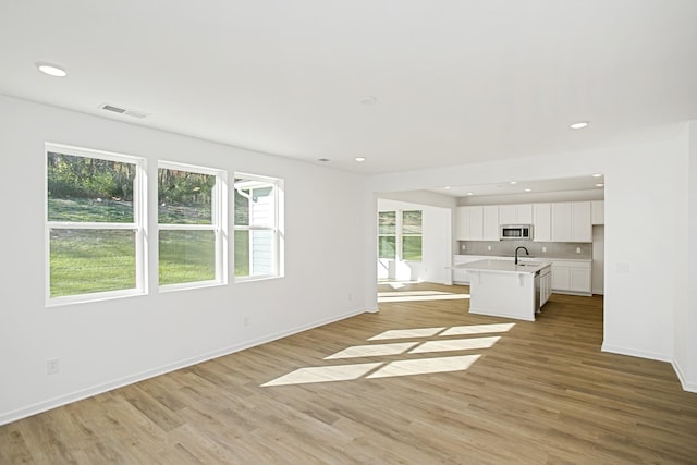 unfurnished living room with recessed lighting, a sink, and light wood-style floors