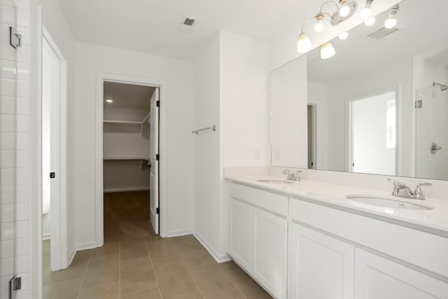 bathroom featuring a walk in closet, visible vents, a sink, and tiled shower