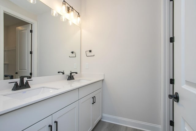 bathroom featuring wood finished floors, a sink, baseboards, and double vanity