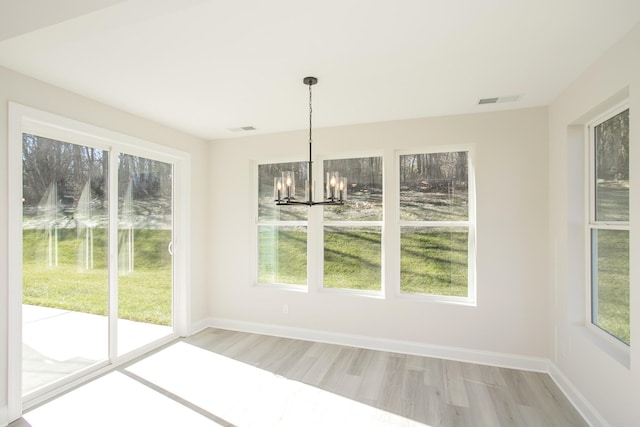 unfurnished dining area featuring visible vents, light wood-style flooring, baseboards, and an inviting chandelier