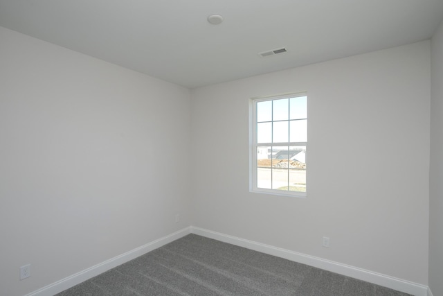 unfurnished room with visible vents, dark carpet, and baseboards