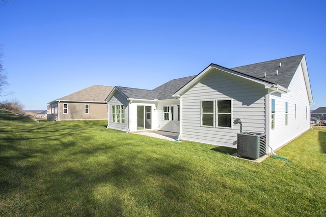 rear view of house with central air condition unit, a shingled roof, and a yard