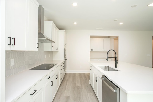 kitchen with a sink, wall chimney range hood, appliances with stainless steel finishes, backsplash, and light wood finished floors