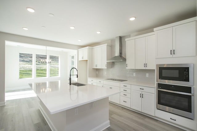 kitchen with black electric stovetop, a sink, stainless steel oven, built in microwave, and wall chimney exhaust hood