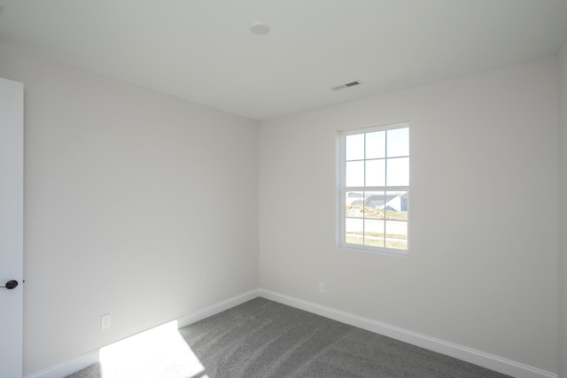 spare room featuring visible vents, dark carpet, and baseboards