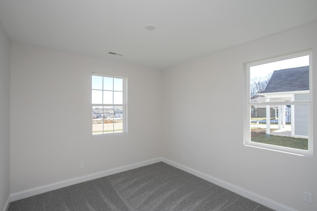 spare room featuring dark colored carpet, visible vents, and baseboards