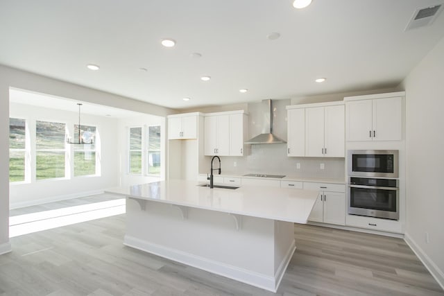 kitchen featuring stainless steel appliances, visible vents, white cabinets, a sink, and wall chimney range hood