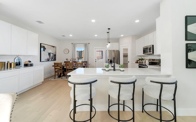 kitchen with visible vents, light wood-type flooring, a breakfast bar, white cabinetry, and appliances with stainless steel finishes