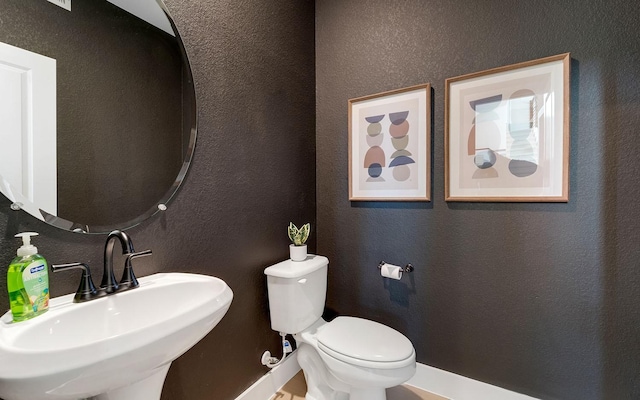 half bathroom with a sink, toilet, and a textured wall