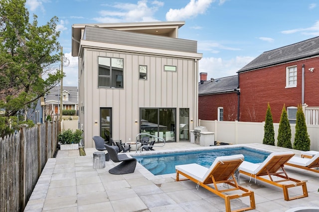 rear view of house with board and batten siding, a fenced in pool, a patio area, and a fenced backyard