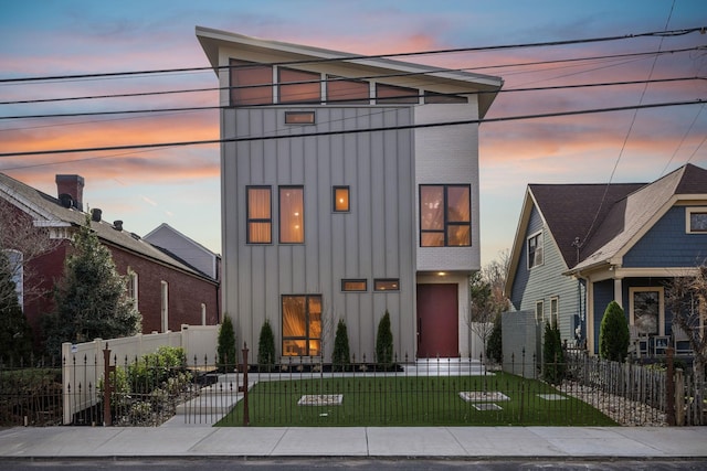 view of front of house with board and batten siding, a fenced front yard, and a front lawn