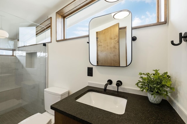 bathroom with tiled shower, vanity, and toilet