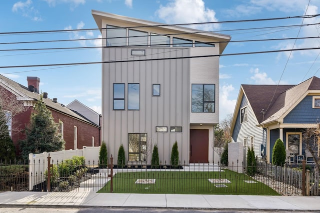 modern home with board and batten siding, a front yard, and a fenced front yard