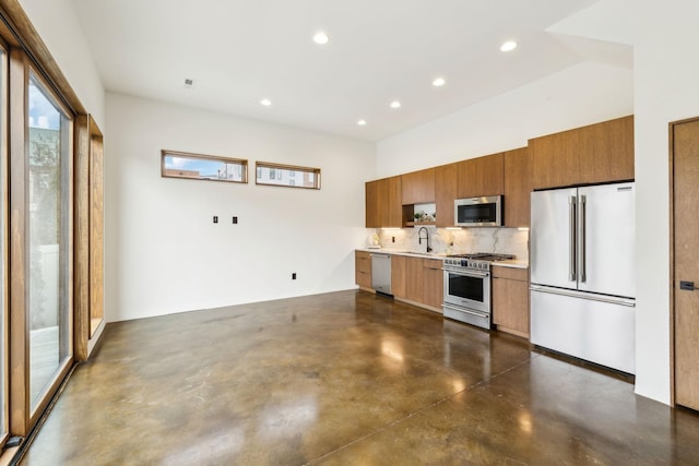 kitchen with concrete floors, a sink, high quality appliances, light countertops, and brown cabinetry