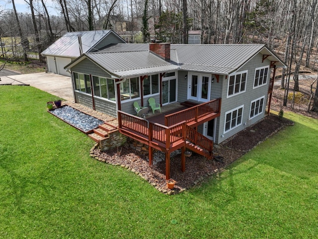 rear view of property featuring concrete driveway, a yard, a sunroom, and a chimney