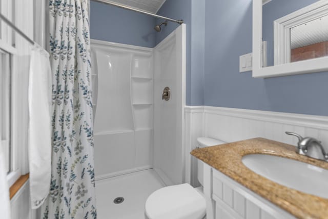 full bathroom featuring wainscoting, toilet, vanity, and a stall shower