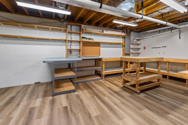 unfinished basement featuring concrete block wall, wood finished floors, and a workshop area