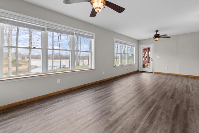 empty room featuring baseboards, a ceiling fan, wood finished floors, and a water view