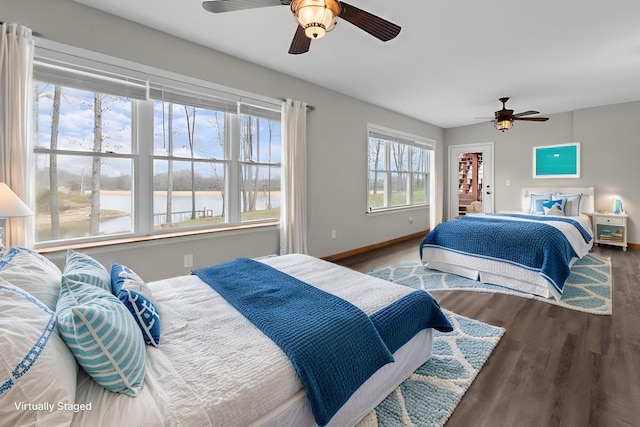 bedroom featuring wood finished floors, a water view, a ceiling fan, and baseboards