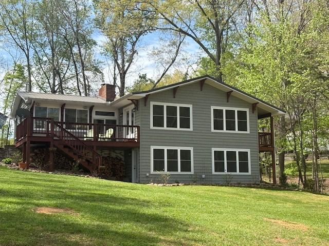 rear view of house with a chimney, stairway, a deck, and a lawn
