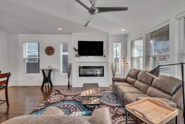 living room with a glass covered fireplace, wood finished floors, a ceiling fan, and baseboards