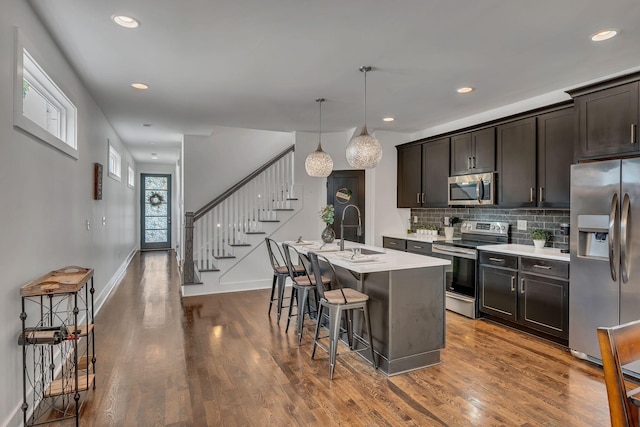 kitchen featuring a breakfast bar, dark wood finished floors, a center island with sink, stainless steel appliances, and a sink