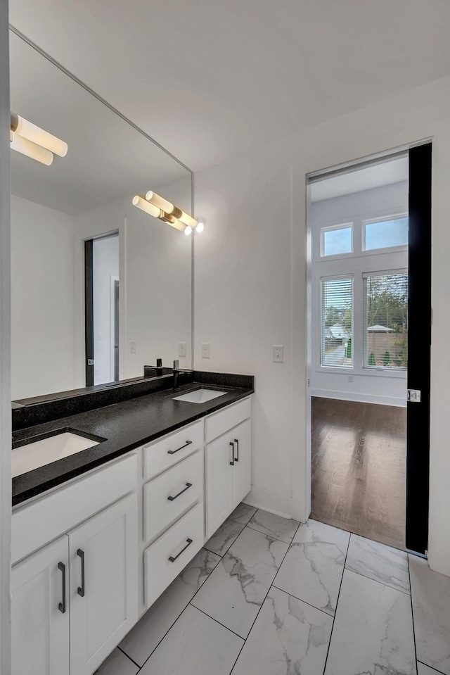 bathroom featuring marble finish floor, double vanity, a sink, and baseboards