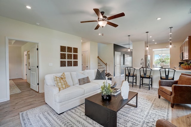 living area with light wood-type flooring, ceiling fan, stairway, and recessed lighting