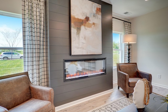 sitting room featuring a glass covered fireplace, visible vents, baseboards, and wood finished floors