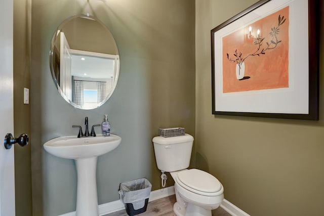 half bath featuring toilet, baseboards, and a sink