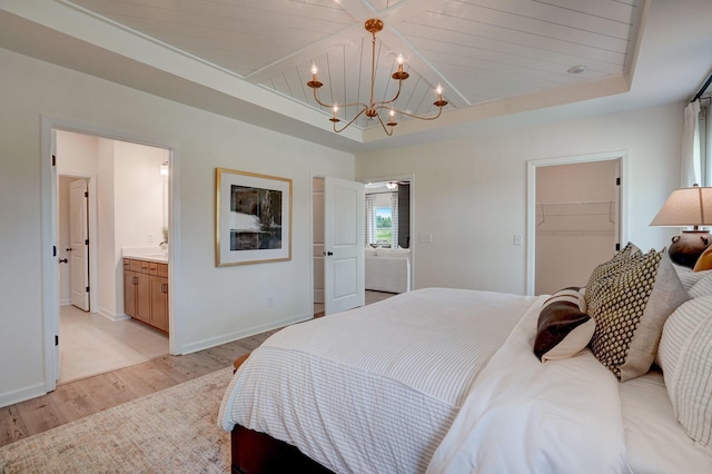 bedroom with a tray ceiling, light wood finished floors, a spacious closet, an inviting chandelier, and baseboards