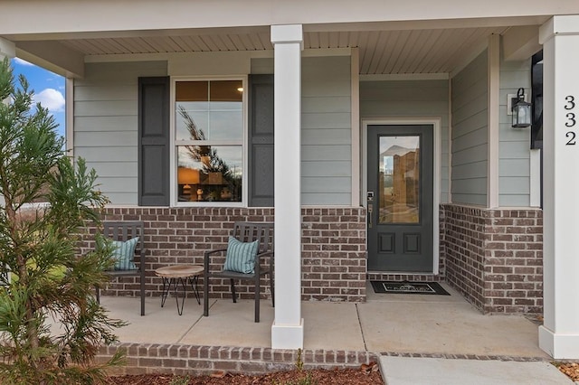 entrance to property featuring a porch and brick siding