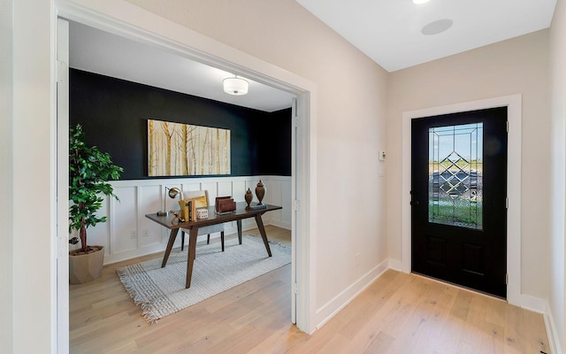 entrance foyer featuring a decorative wall, wainscoting, and light wood finished floors